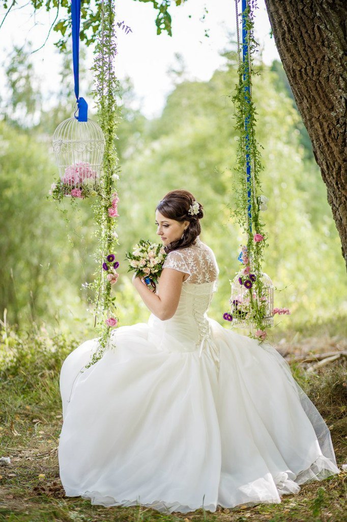 Невеста на качелях, украшенных цветами, раститльностью и винтажными клетками